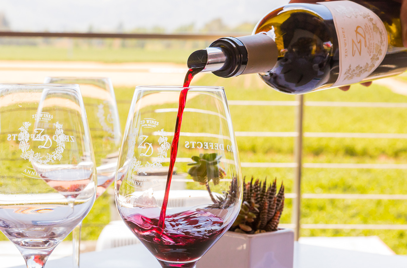 Red ZD wine being poured into a ZD Wines glass with the Rutherford vineyard view in the background