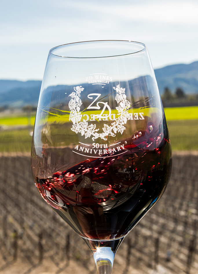 ZD red wine swirling in a glass overlooking Rutherford vineyards