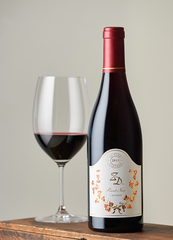 A bottle of ZD Pinot Noir on a wooden box with a full glass of wine behind it