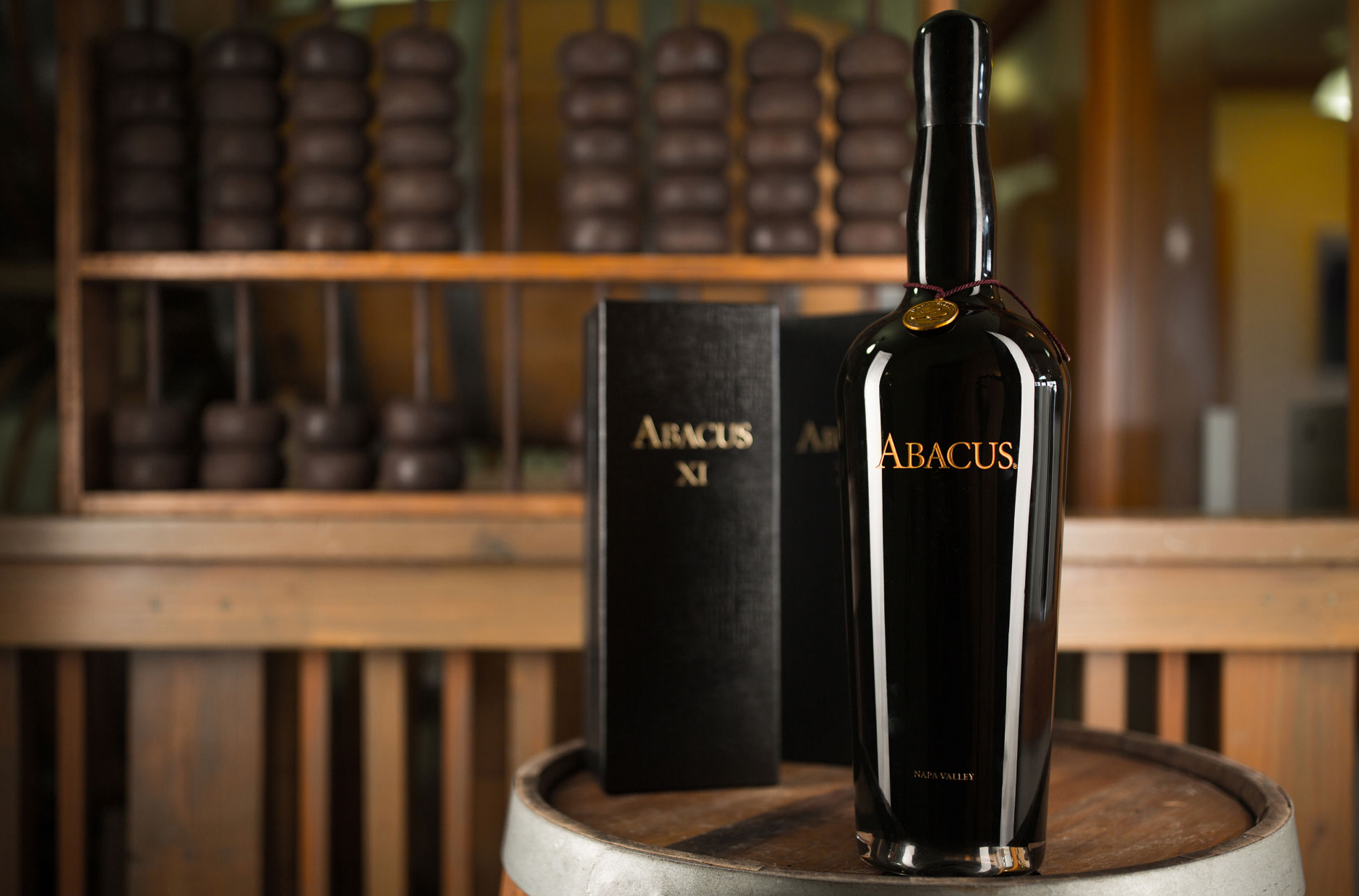 A bottle of Abacus on a barrel with its box and a giant abacus replica in the background.